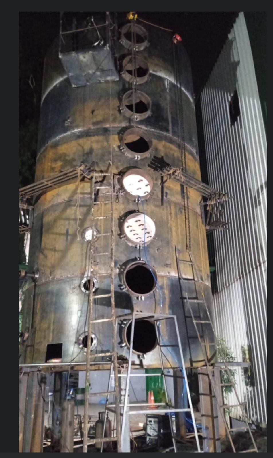 Tall cylindrical steel process vessel with multiple nozzle openings under fabrication